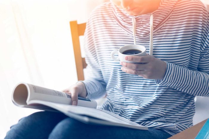 person reading a magazine and drinking a cup of coffee