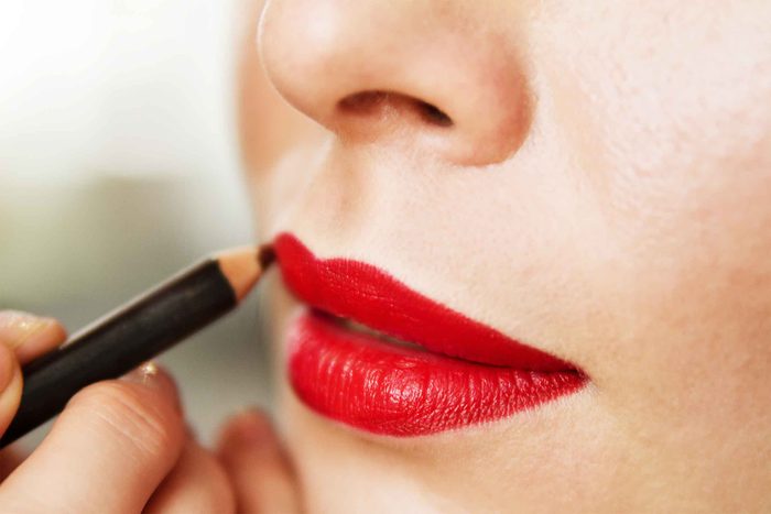 Woman applying red lip liner to red lips.