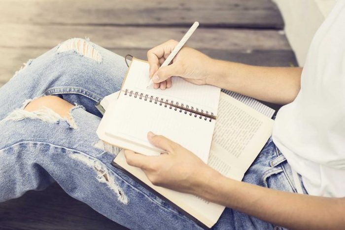 Woman in torn jeans writing in a journal with a pen.