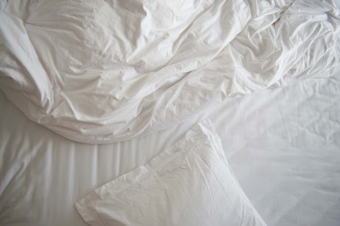 unmade bed with white pillow, blanket, and comforter