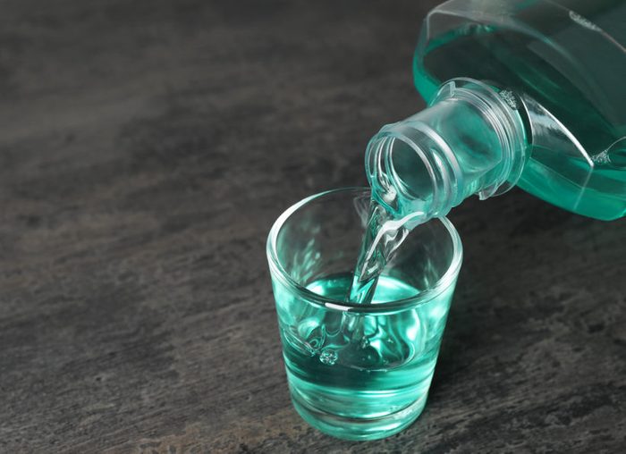 Pouring mouthwash in glass and space for text on dark background. Teeth care