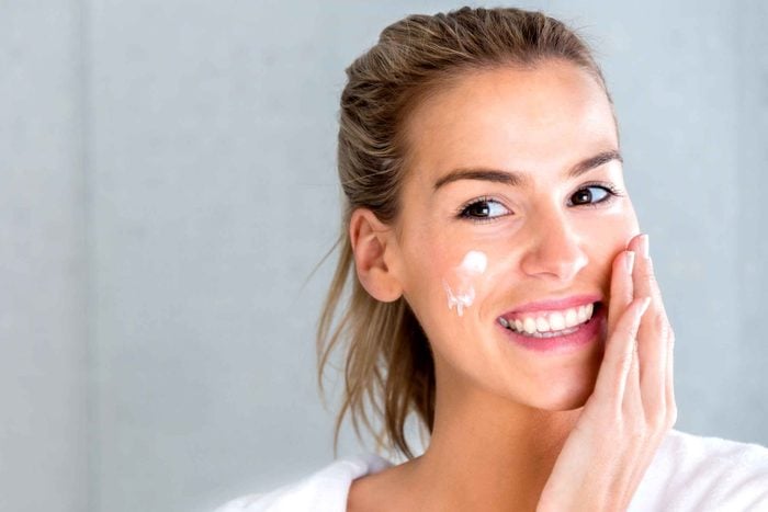 smiling woman applying face cream 