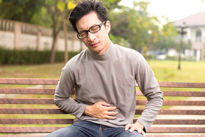 man sitting on a park bench holding his stomach and wincing