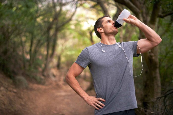 man on a trail drinking from water bottle