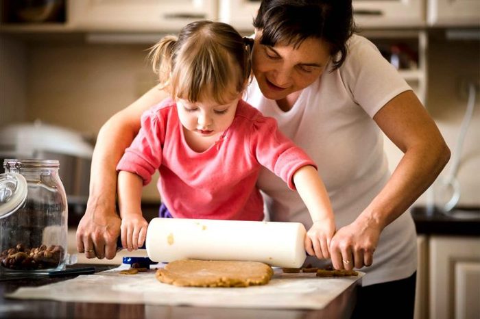 Mother and daughter rolling out dough with a rolling pin in the kitchen.