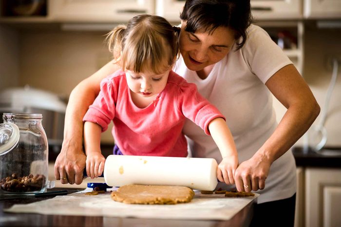 Mother and daughter rolling out dough with a rolling pin in the kitchen.