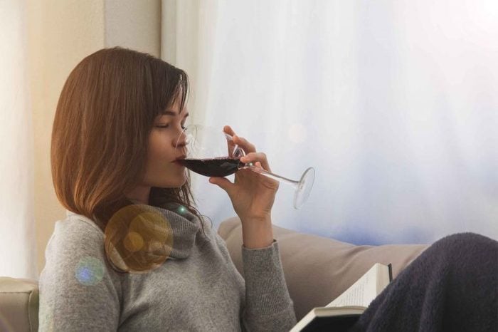 Woman reading a book on the couch drinking red wine.