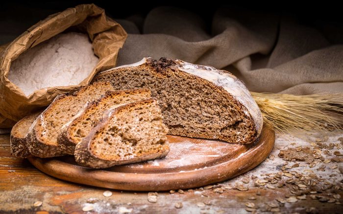 dark brown bread on board with bag of flour
