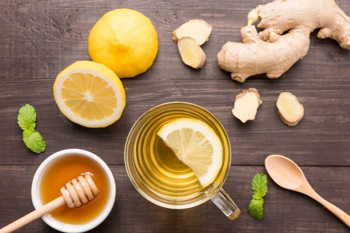 mug of tea with lemon surrounded by lemon, ginger, honey, and mint
