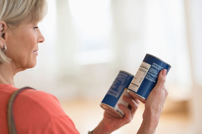 woman reading nutrition label on two cans of food
