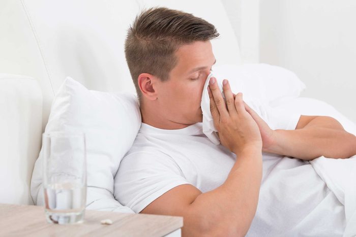 Man blowing his nose with a tissue in bed.