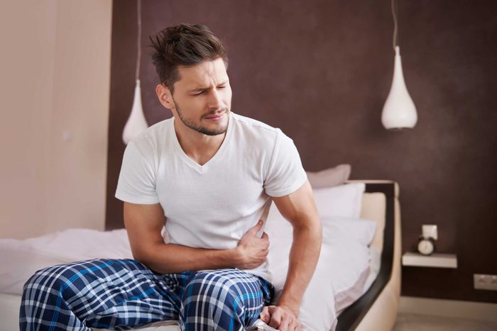 man in pajamas sitting on the edge of a bed and holding his stomach in pain