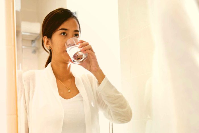 woman taking sip of water from glass in front of mirror