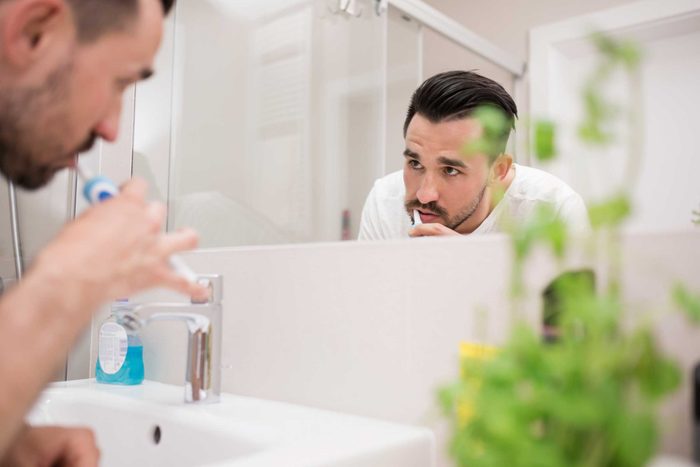 man brushing teeth and looking in mirror