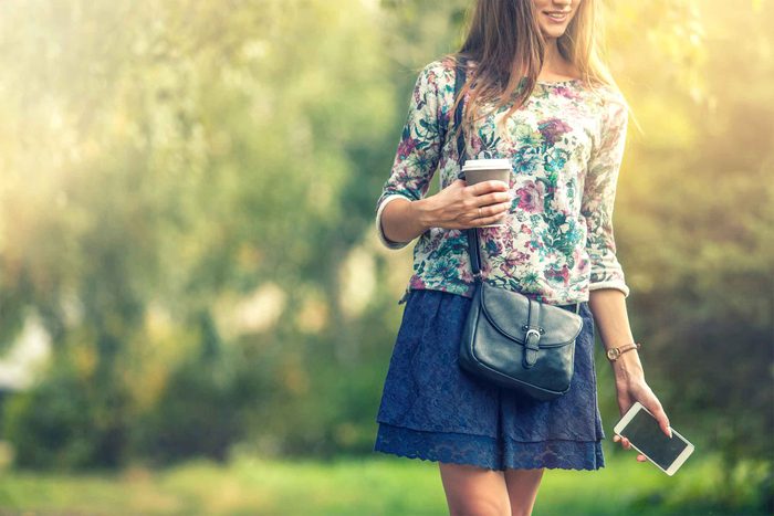 woman walking and holding a phone and a coffee cup