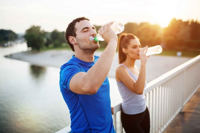  Exercising man and woman stop on a footbridge over a body of water to drink from their water bottles.