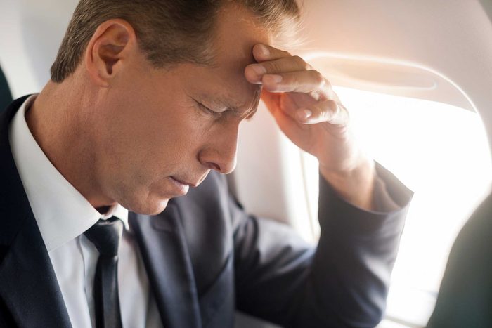man in business suit on airplane with hand on head
