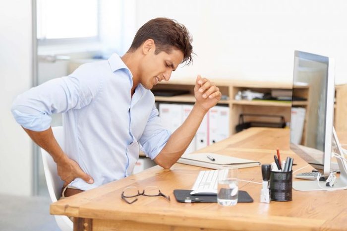 Man at a desk holding his back.