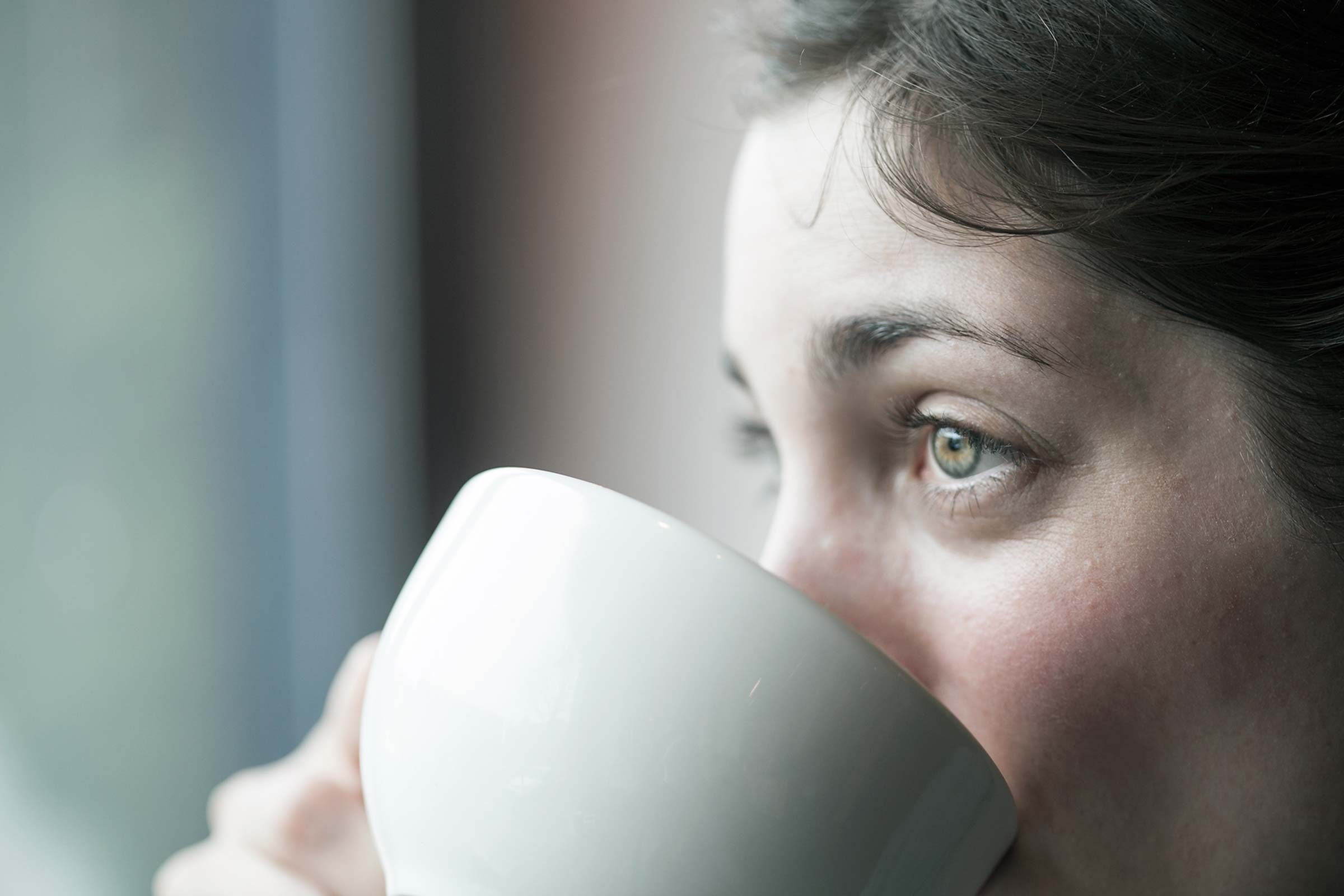 Woman with pale complexion sipping from a mug.