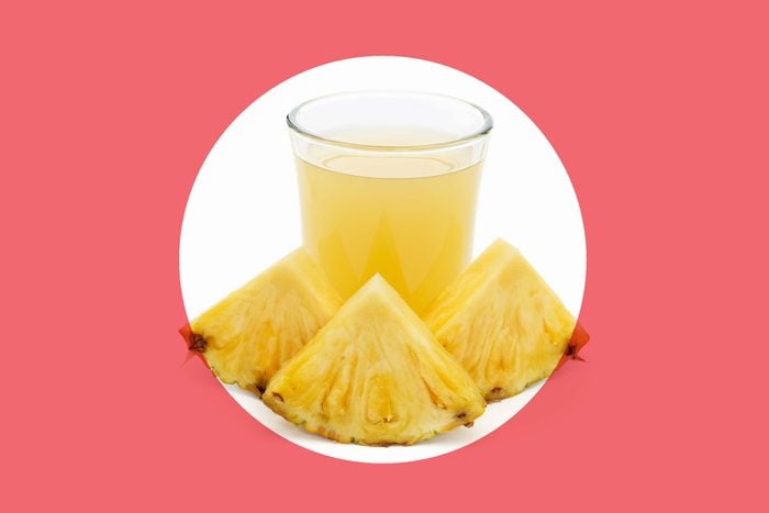 glass of pineapple juice with three wedges of pineapple