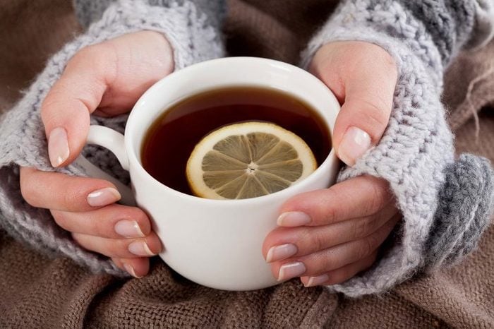 Woman in a sweater holding a cup of tea with a lemon slice.