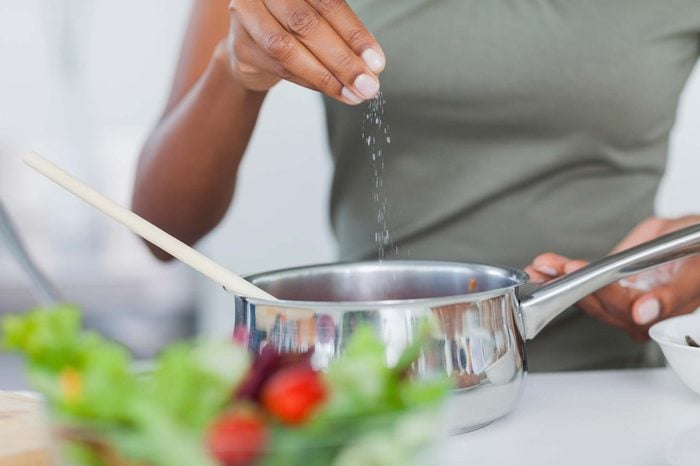 Woman adding salt to saucepan