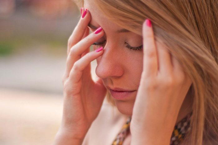 Woman with pink nailpolish holding her head as if tired.