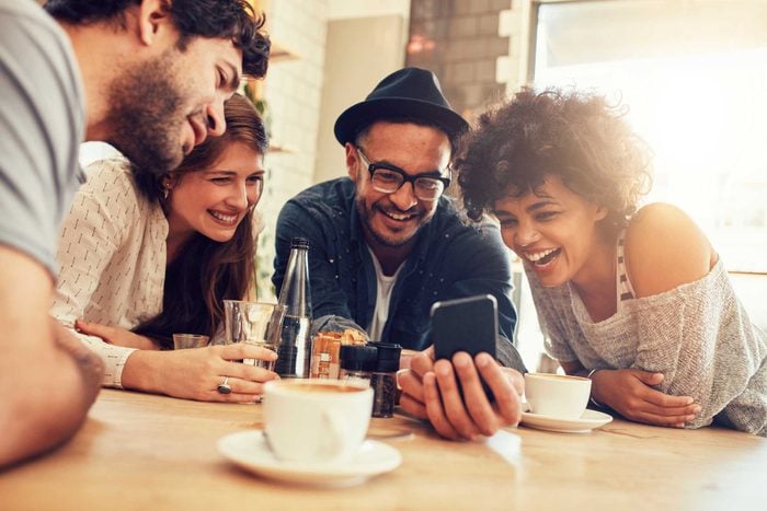 group of four people looking at smartphone and laughing