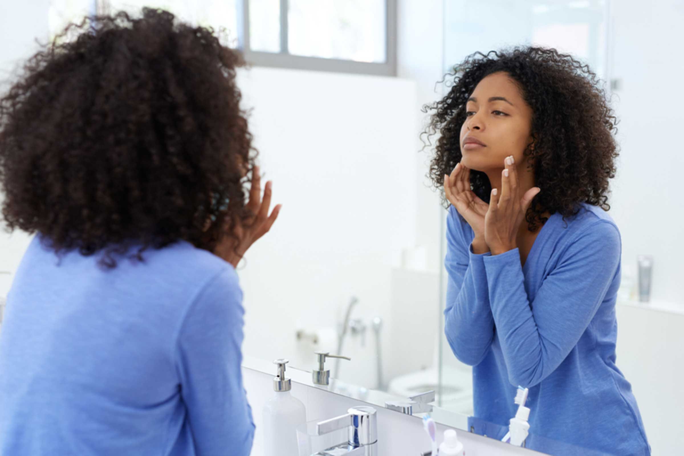 woman applying product on her face in mirror