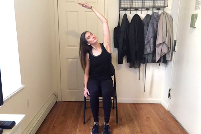 Woman sitting in a chair doing an overhead stretch.