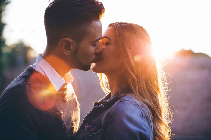 Woman and man kissing behind a sunset.