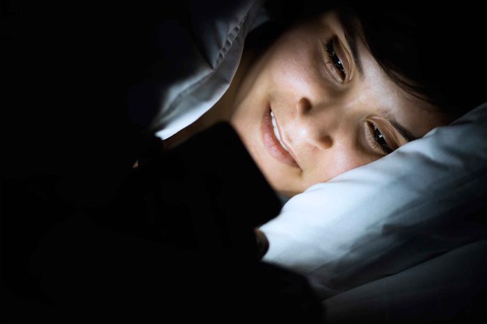 Woman looking at phone screen while lying in bed