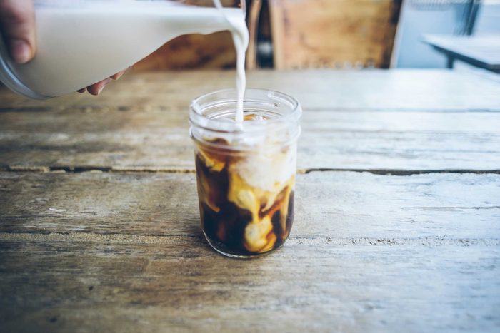 pitcher of milk pouring into glass of iced coffee