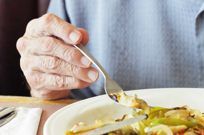 elderly person's hand holding a fork over meal