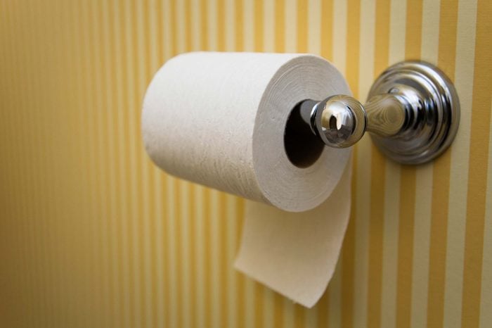 Toilet paper roll mounted on a yellow and white wallpapered bathroom wall.