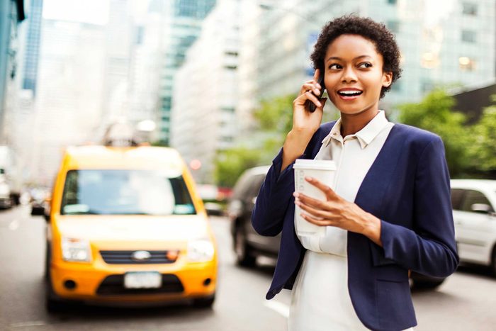 woman on street with to-go coffee, talking on cell phone