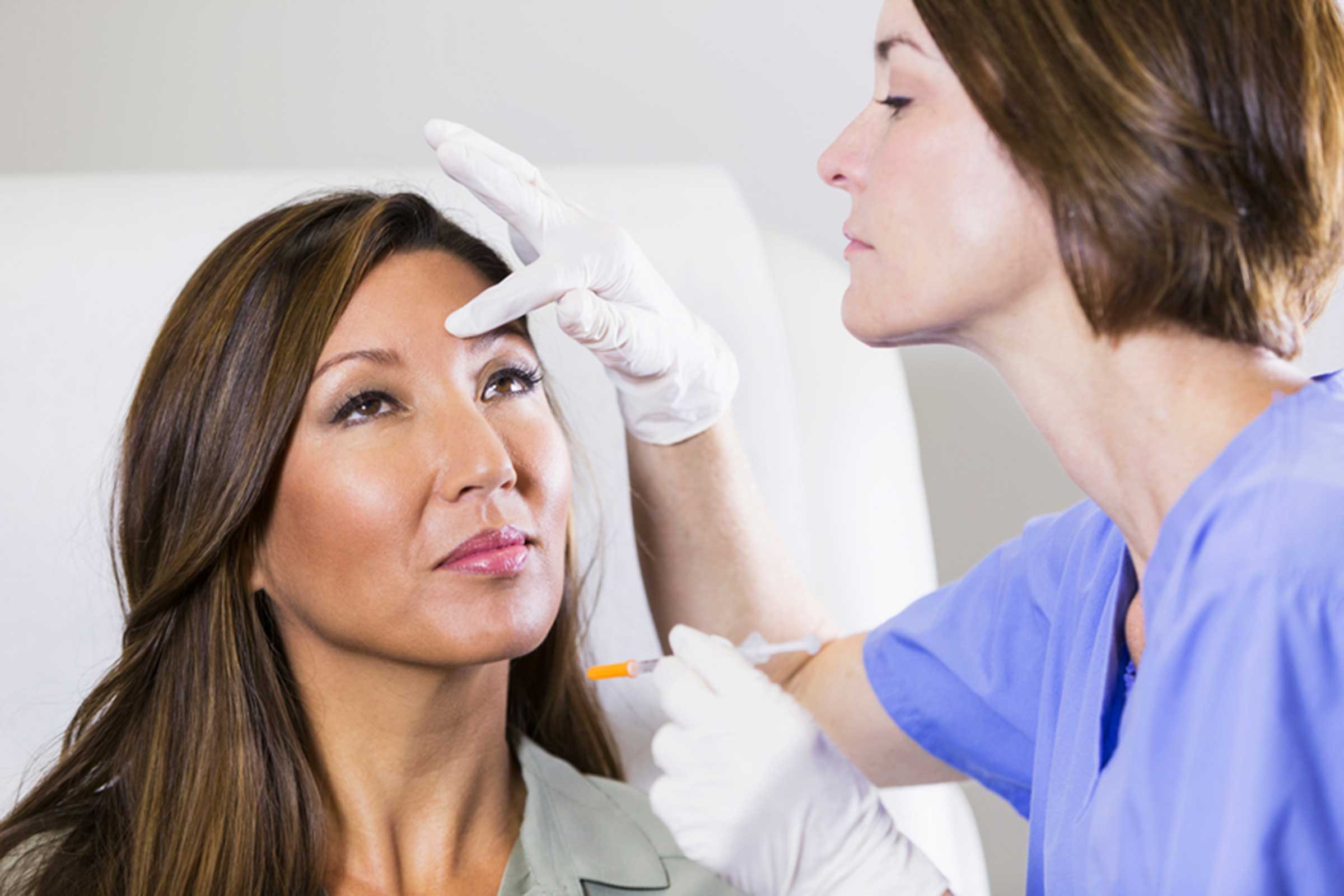 dermatologist with needle, touching woman's face