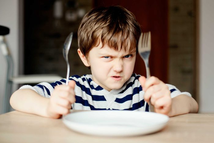 Angry child holding fork and knife in front of dinner plate