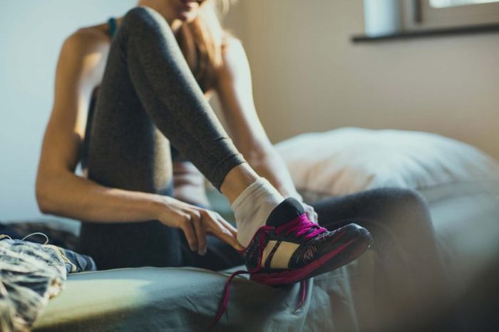 woman sitting on bed putting on athletic shoes
