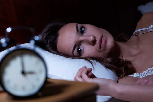 Wide-awake woman looking at her nightstand clock.