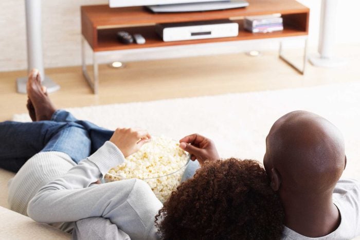 Man and woman curled up on the couch together eating from a bowl of popcorn.