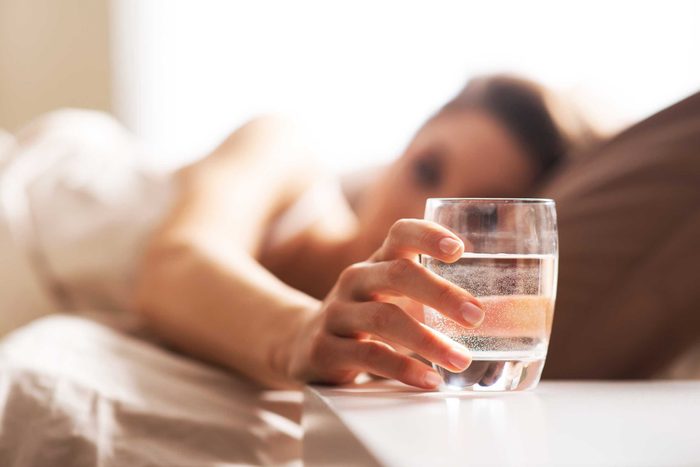 Woman in bed reaching for a glass on water on her nightstand.