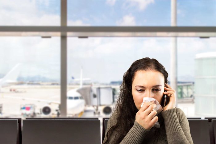 woman at the airport on the phone, blowing her nose into a tissue