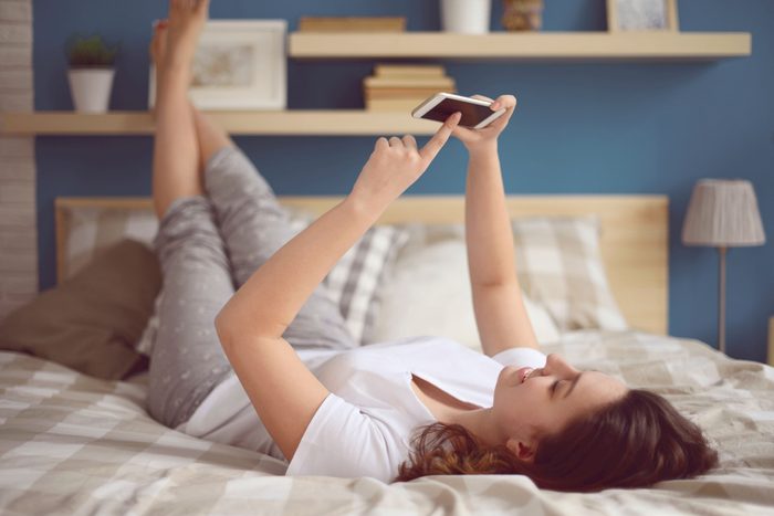 woman lying on bed looking at phone