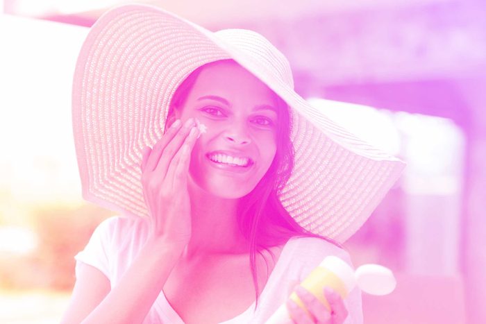 woman in a sun hat, smiling and applying sunscreen