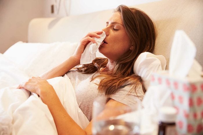 Woman blowing her nose in bed.