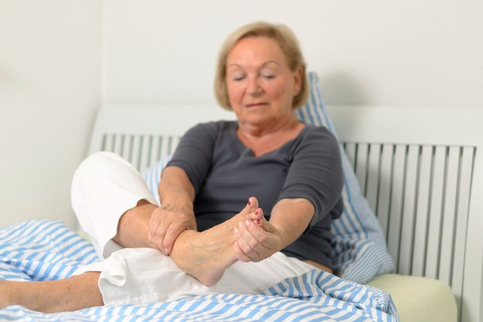 woman sitting in bed holding her foot
