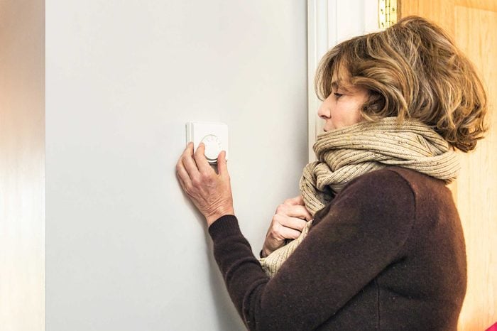 Woman in a scarf turning up the thermostat at her house.