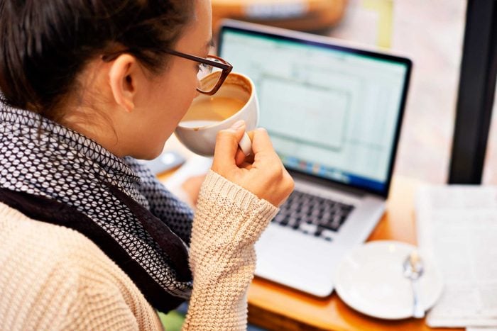 woman sipping coffee while working on laptop