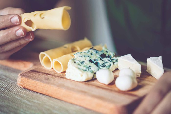 Swiss cheese, blue cheese, brie cheese, and mozzarella balls arranged on a wooden platter, with a man sampling the Swiss cheese.